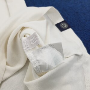 Puede incluir: Camiseta blanca con una etiqueta gris que dice "UNIQLO".