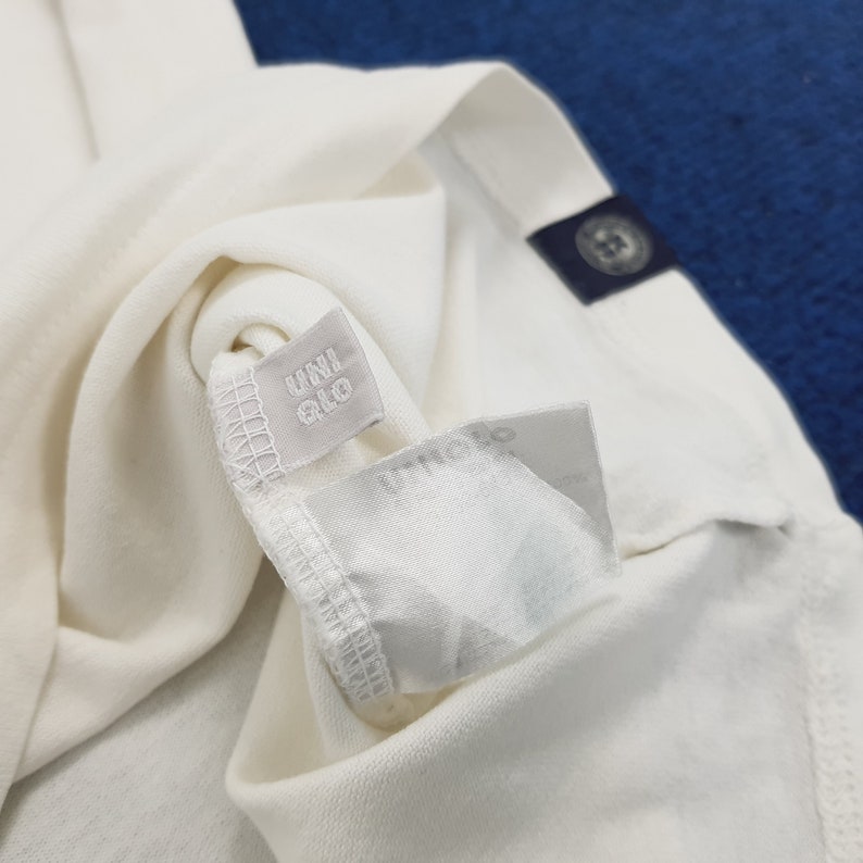 Puede incluir: Camiseta blanca con una etiqueta gris que dice "UNIQLO".