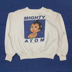 May include: White sweatshirt featuring a graphic of Astro Boy with the text "MIGHTY ATOM" in blue. The cartoon character is depicted with black hair, a red face, and a green outfit. The sweatshirt has long sleeves and a crew neck.