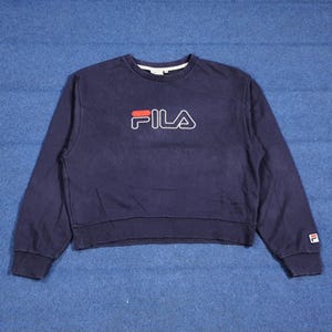Puede incluir: Sudadera azul marino con el nombre de la marca "FILA" en letras rojas y blancas en el pecho. La sudadera tiene cuello redondo, mangas largas y un peque&ntilde;o logotipo en el pu&ntilde;o de la manga izquierda. La prenda es de material suave.