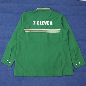 Puede incluir: Camisa de trabajo verde de manga larga con el texto "7-ELEVEN" en blanco en la espalda. La camisa tiene un diseño a rayas en rojo, blanco y naranja. El cuello y los puños tienen botones blancos.