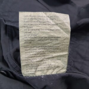 May include: Close-up of a care label attached to a navy blue garment. The label, with English and French text, provides washing and care instructions, including dry cleaning, line drying, and avoiding steam. The fabric's color and texture may change with wear.