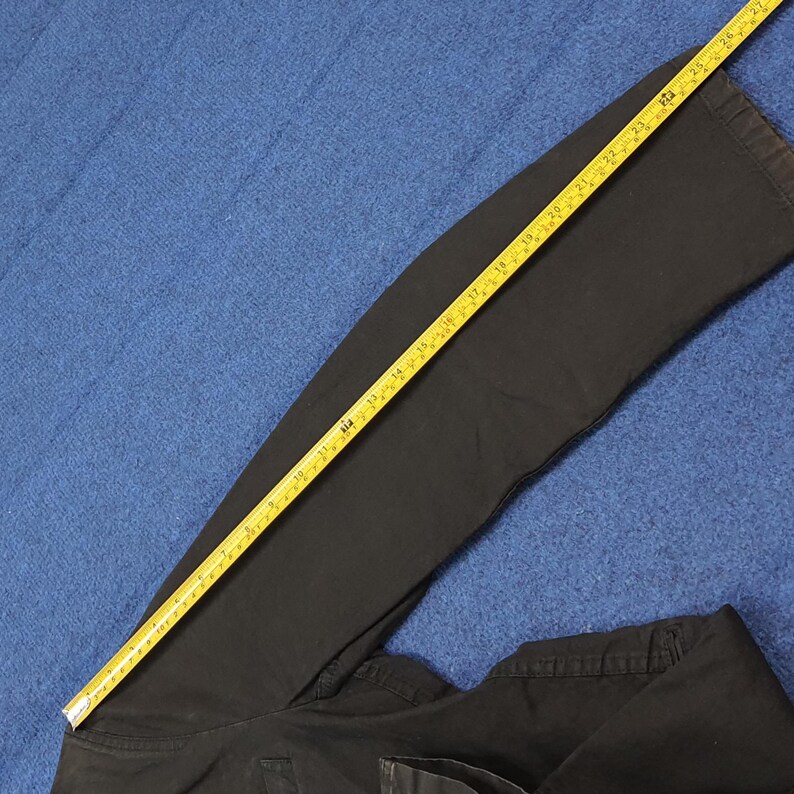 May include: Black pants with a yellow measuring tape laid across the fabric. The measuring tape shows a length of approximately 27 inches. The pants are folded and lying on a blue surface.