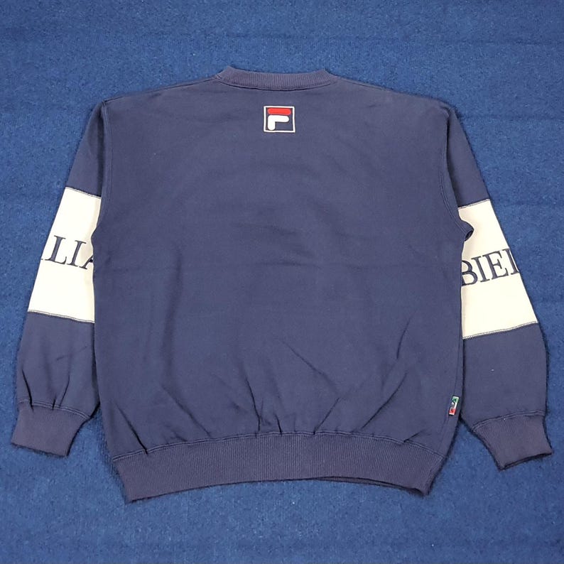 Puede incluir: Sudadera azul marino con mangas blancas. La manga izquierda tiene la palabra "ITALIA" y la derecha "BIELLE". El logotipo de Fila est&aacute; en la parte superior de la espalda. La sudadera tiene dobladillo y pu&ntilde;os acanalados.