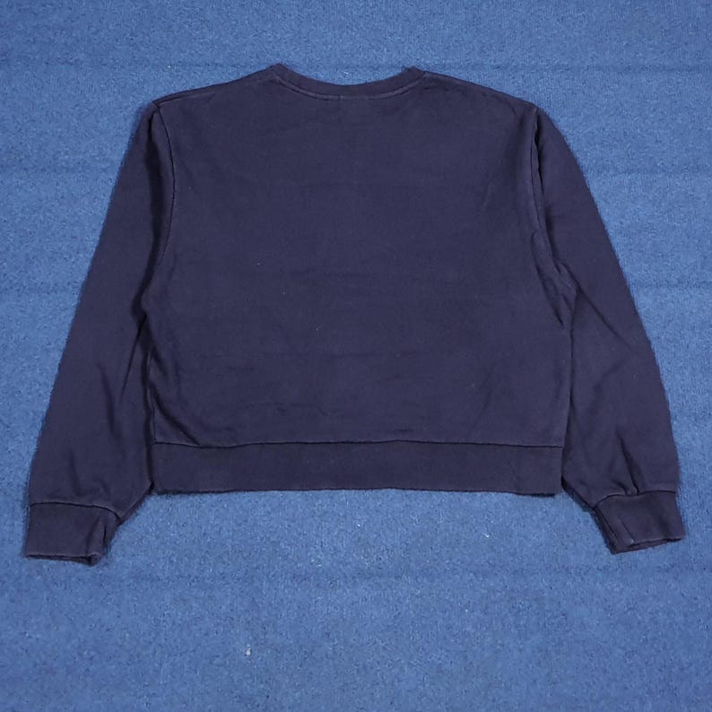 Puede incluir: Una sudadera azul marino con cuello redondo y mangas largas. La sudadera est&aacute; recortada en la cintura y tiene pu&ntilde;os y dobladillo acanalados. La tela parece ser un material suave y c&oacute;modo.