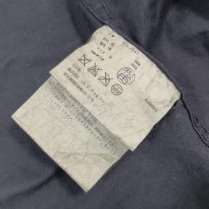 May include: Close-up of a navy blue garment with a tag attached. The tag has Japanese text, care symbols, and the text "AD2004". The tag is attached to the garment with a seam.