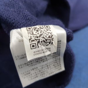 Puede incluir: Primer plano de una tela azul marino con una etiqueta blanca adjunta. La etiqueta presenta un c&oacute;digo QR, los n&uacute;meros 4946903866 y 0000246818, y texto en japon&eacute;s.