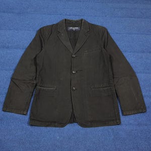 May include: A black blazer with three buttons and two front pockets. The blazer has a notched lapel and long sleeves. The label on the inside of the blazer is visible.