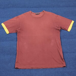 May include: A maroon short-sleeved t-shirt with yellow sleeve cuffs. The shirt has a crew neck and a horizontal seam across the chest. The shirt is made of a soft material.