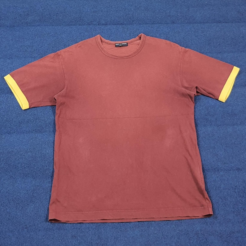 May include: A maroon short-sleeved t-shirt with yellow sleeve cuffs. The shirt has a crew neck and a horizontal seam across the chest. The shirt is made of a soft material.