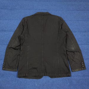 May include: Black blazer with a classic design. The jacket features a notched lapel, three-button closure, and multiple pockets. The back of the jacket has a center vent for added comfort. The blazer is made of a durable fabric and is suitable for various occasions.