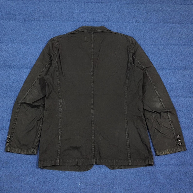 May include: Black blazer with a classic design. The jacket features a notched lapel, three-button closure, and multiple pockets. The back of the jacket has a center vent for added comfort. The blazer is made of a durable fabric and is suitable for various occasions.