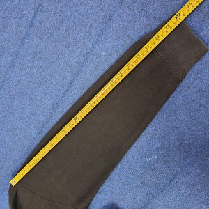 K&ouml;nnte beinhalten: Ein schwarzer Sweatshirt-&Auml;rmel wird mit einem gelben Ma&szlig;band gemessen. Das Ma&szlig;band zeigt eine L&auml;nge von etwa 63,5 cm. Der &Auml;rmel liegt auf einer blauen Oberfl&auml;che.