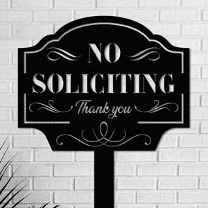 K&ouml;nnte beinhalten: Schwarzes Metallschild mit den Worten "NO SOLICITING" und "Thank you" in Wei&szlig;. Das Schild hat einen verzierten Rahmen und ist auf einem schwarzen Pfahl montiert, geeignet f&uuml;r den Garten.