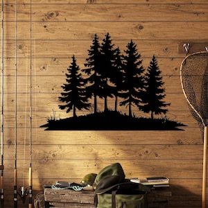 May include: A black metal wall art piece featuring a silhouette of a cluster of pine trees growing on a small grassy hill. The design displays detailed branches and needles, creating a sharp contrast against the wooden wall background.