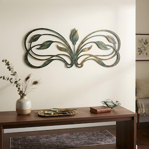 May include: A horizontal metal wall art piece featuring a central tulip bud flanked by symmetrical, flowing vine and leaf motifs. The metal has a weathered, multi-toned finish with shades of dark green, bronze, and copper throughout the design.