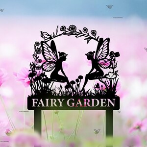 Puede incluir: Silueta negra de metal de dos hadas sentadas bajo un arco floral con el texto "FAIRY GARDEN" en un letrero debajo. Las hadas se miran y tienen alas y flores en el pelo.