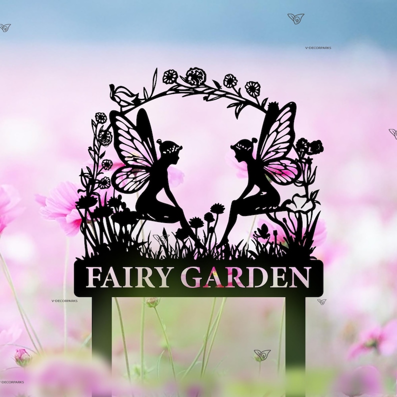 Puede incluir: Silueta negra de metal de dos hadas sentadas bajo un arco floral con el texto "FAIRY GARDEN" en un letrero debajo. Las hadas se miran y tienen alas y flores en el pelo.