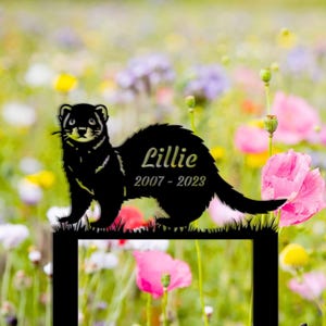 May include: Black metal silhouette of a ferret with the name "Lillie" and the dates "2007 - 2023" engraved on it. The silhouette is placed in a field of wildflowers.