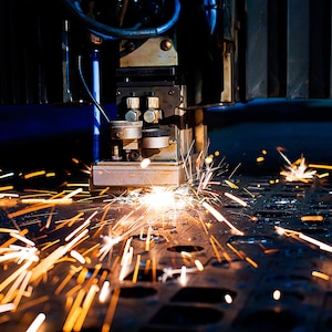 Puede incluir: Primer plano de una m&aacute;quina de corte por l&aacute;ser en funcionamiento, con chispas que salen del metal que se est&aacute; cortando.