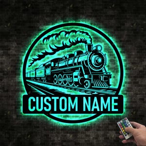 May include: A black metal train silhouette with a custom name plate, illuminated by a green LED light within a circular frame. The image features a detailed train design with smoke and tracks, set against a brick wall background.