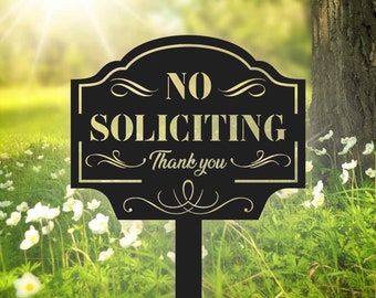 May include: Black metal garden sign with the words "NO SOLICITING" and "Thank you" in gold lettering. The sign is set in a garden with green grass, white flowers, and a tree trunk in the background.