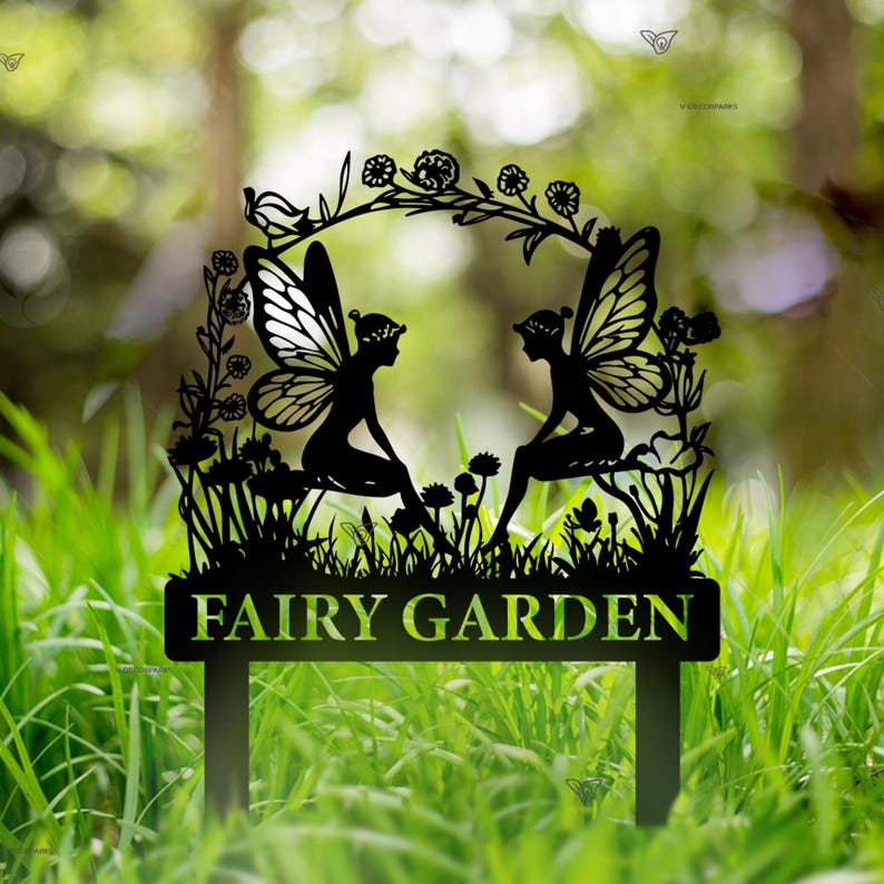 Puede incluir: Estaca de jard&iacute;n de metal negro con dos hadas sentadas en una rama con flores y hojas. La estaca tiene un letrero que dice "FAIRY GARDEN".