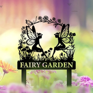 Puede incluir: Silueta negra de metal de dos hadas sentadas en un jard&iacute;n con flores y hojas. El letrero dice "Fairy Garden".