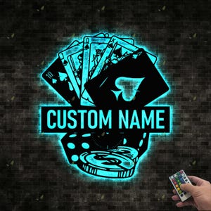 May include: Black metal wall art featuring playing cards, dice, and poker chips, illuminated with a blue glow. The text "CUSTOM NAME" is displayed prominently. The art is set against a dark brick wall.