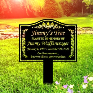 May include: Black memorial sign with gold trim and text that reads "Jimmy's Tree, Planted in Memory of Jimmy Waffentrager, January 6, 1973 - November 23, 2025." The sign is in a grassy area.