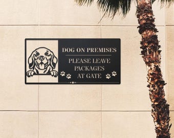 Può includere: Un cartello in metallo nero con una silhouette bianca di un cane e il testo "DOG ON PREMISES PLEASE LEAVE PACKAGES AT GATE" con impronte di zampe su entrambi i lati del testo.
