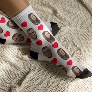 Könnte beinhalten: Weiße Socken mit einem Muster aus roten Herzen und Gesichtern. Die Socken werden an den Füßen einer Person getragen.