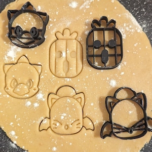 Könnte beinhalten: Nahaufnahme eines Blechs mit Keksteig, auf dem fünf Ausstecher liegen. Die Ausstecher sind in Form von Ananas, Katze, Igel, Waschbär und Fledermaus. Der Teig ist leicht mit Mehl bestäubt.