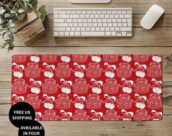 Può includere: Un tappetino da scrivania rosso con un motivo bianco ripetuto di torte e fiocchi. Il tappetino ha il testo "FREE US SHIPPING" e "AVAILABLE IN FOUR SIZES" in un cerchio nero. Sono visibili una tastiera, un mouse e una pianta.