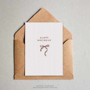 May include: A white card with a pink ribbon bow and the text "Happy Birthday" in red. The card is on a brown envelope.