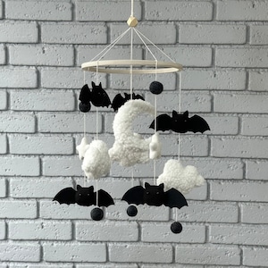 May include: A black and white baby mobile with bats, clouds, and stars. The mobile is hanging from a wooden ring.