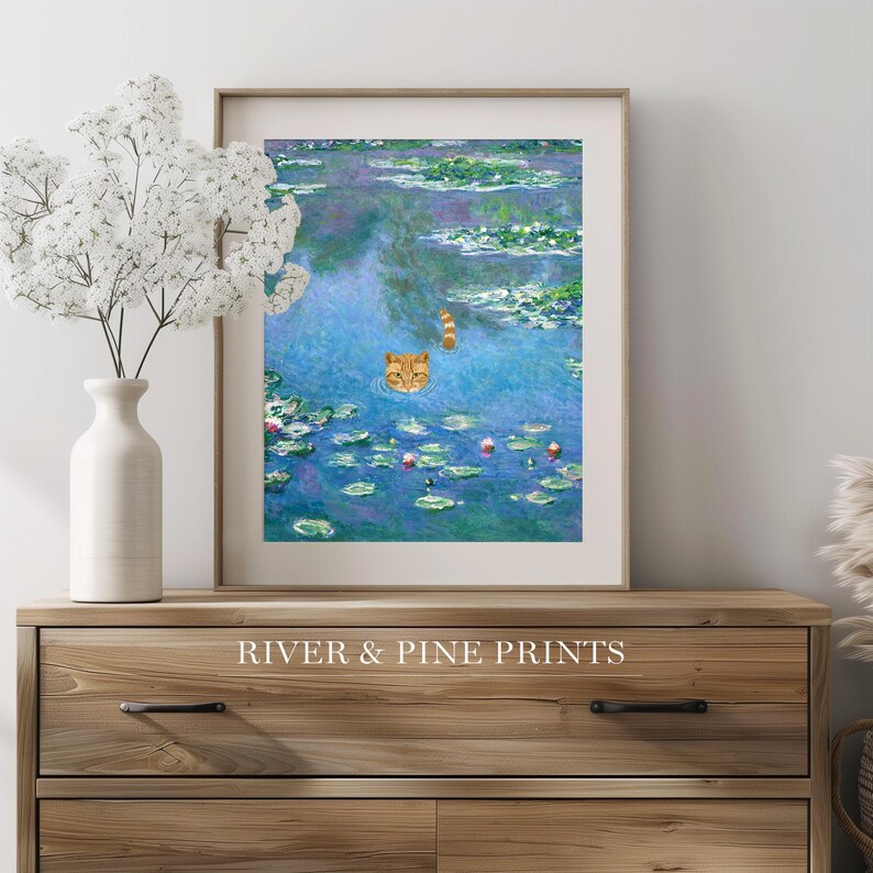 May include: A framed print of a painting depicting a cat swimming in a pond with water lilies. The cat is orange and white and is looking directly at the viewer. The pond is blue and green with pink flowers. The print is framed in a white frame and has the text "River & Pine Prints" at the bottom.