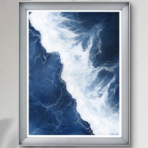 May include: A framed abstract painting of a blue and white ocean wave. The wave is painted in a realistic style, with white foam crashing against the blue water. The painting is framed in a silver frame.