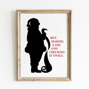 May include: Framed print featuring a black silhouette of Santa Claus holding a long scroll. The text "HE'S MAKING A LIST AND CHECKING IT TWICE" is in red. The frame is a light brown color.
