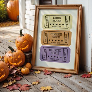 Puede incluir: Una impresión enmarcada con tres boletos de estilo vintage para un laberinto de maíz, un campo de calabazas y una casa embrujada. Los boletos son amarillos, naranjas y morados. Calabazas talladas con caras iluminadas y hojas de otoño.