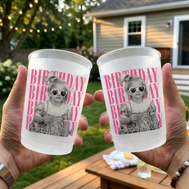 May include: Two frosted plastic cups with a pink and white design. The cups feature the text "BIRTHDAY" and a black and white image of a girl wearing heart-shaped sunglasses. The text "Sophia's 18th" is also printed on the cups.