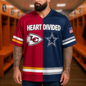 Op de afbeelding: Een shirt met een gespleten ontwerp, met een rode linkerkant met een wit pijlpuntlogo en een blauwe rechterkant met een wit sterlogo. De tekst HEART DIVIDED staat op de borst gedrukt. De mouwen hebben strepen en op de rechtermouw staat een kleine Amerikaanse vlag.