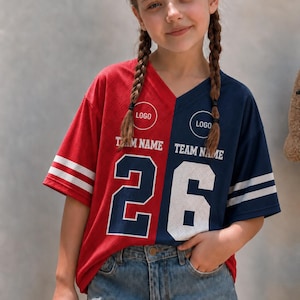 Könnte beinhalten: Ein zweifarbiges V-Ausschnitt-Trikot mit einer roten linken Seite und einer marineblauen rechten Seite. Das Shirt zeigt den Text "LOGO" und "TEAM NAME" über der großen Zahl "26" in Weiß und Marineblau. Es hat weiße Streifen an den Ärmeln.