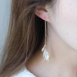 May include: A pair of gold dangle earrings with a delicate chain and clear crystal accents.