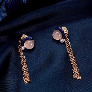 May include: A pair of gold earrings with a blue and white stone and a dangling chain. The earrings are on a dark blue background.