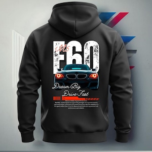 Może przedstawiać: Czarna bluza z kapturem z białym nadrukiem przedstawiającym samoch&oacute;d BMW M5 E60 z tekstem "Dream Big Drive Fast" i "Bimmer Mafia Original Products".