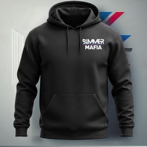 Może przedstawiać: Czarna bluza z kapturem z białym logo, na kt&oacute;rym widnieje napis "Bimmer Mafia" wielkimi literami. Logo znajduje się na środku klatki piersiowej bluzy.