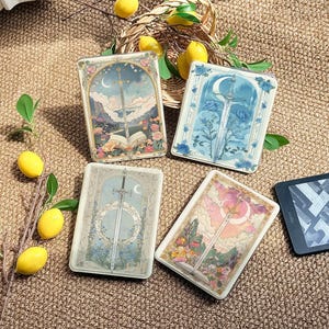 May include: Four rectangular e-reader cases featuring sword and floral illustrations. One case shows a sword over an open book, another a sword with blue roses, a third a sword with a circular frame, and the fourth a sword against a pink sky.