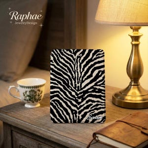 May include: A rectangular electronic reader cover featuring a black and white zebra stripe pattern. The name Evelyn is printed in a white cursive script in the bottom right corner of the cover. The cover has rounded corners and a flat surface.