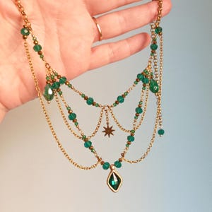 May include: A multi-layered gold chain necklace with green crystal beads and a star charm. The necklace also features a large, faceted green crystal pendant.